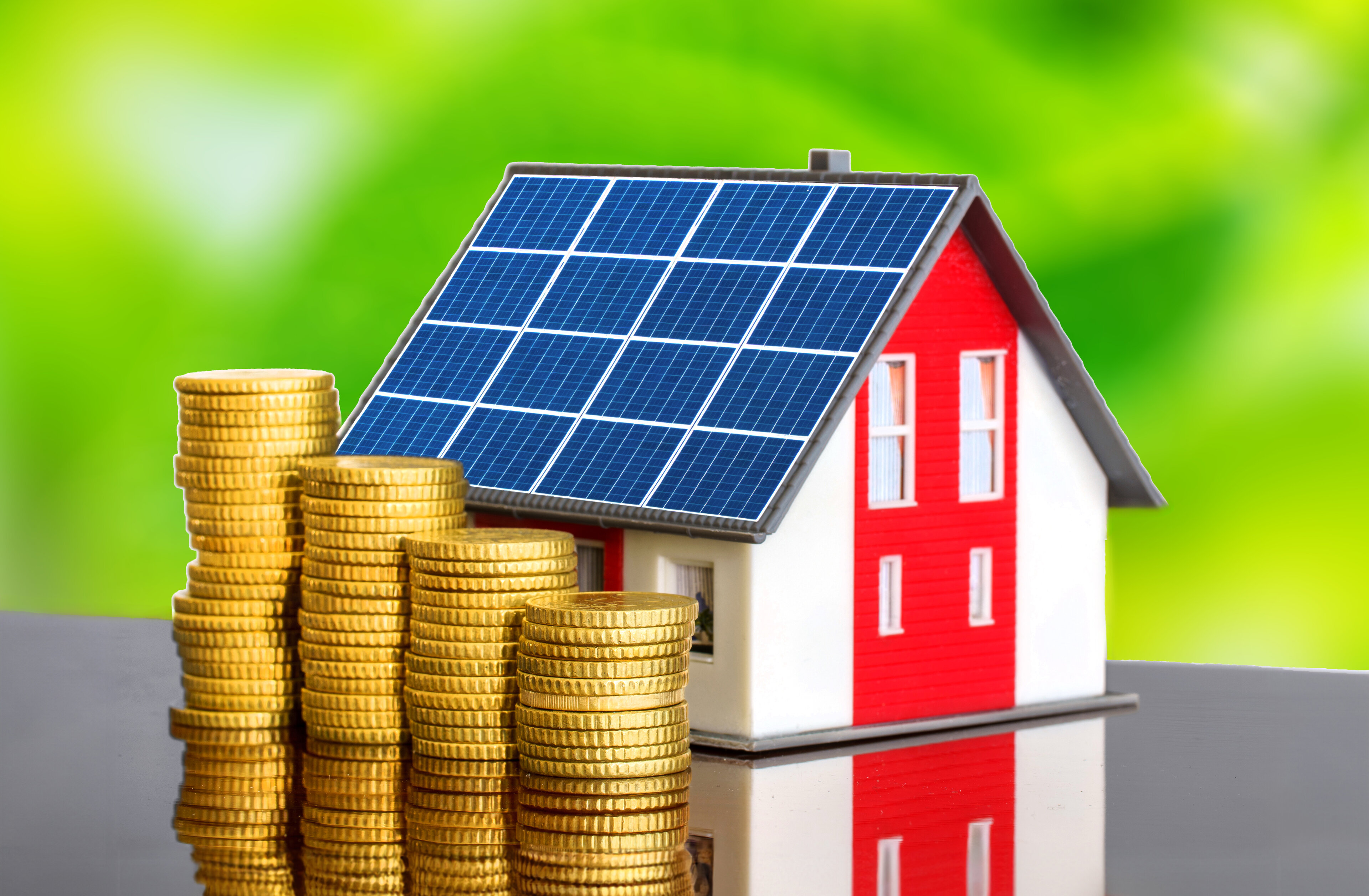 Modell eines energieeffizienten Haus mit Solardach und aufgestapelten Geldstücken